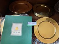 Photo showing 12 lacquered brass chargers stacked with 8 gold Gibson plastic charger plates beside them and original Lacquered Brass branded box.