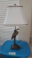 Full view of the lamp showing carved heron standing on turtle, with butterfly in beak and attached lamp shade on top.