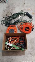 Photo showing two orange extension cord reels and a box filled with various electric cords and power cables.