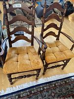 Two captain chairs with arms, wooden ladder back design, surrounded by a living room setting with beige cushioned seats.