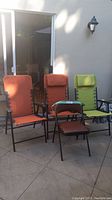 Photo of four folding chairs—three with orange cushions, one with green cushion—all with black metal frames, armrests, and reclining bungee lace design.