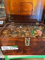 Front view of brown plastic jewelry case showing organized compartments of assorted earrings, pins, bracelets, and beaded necklaces visible through top lid