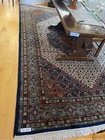 Full view of rectangular wool rug under table showing border and fringe
