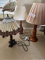 Three lamps on carpet showing one stained glass shade lamp and two wooden base lamps with fabric shades.