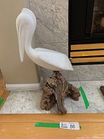 Side view of the pelican sculpture showing the curved neck and positioning on the burl wood base in front of a marble fireplace.