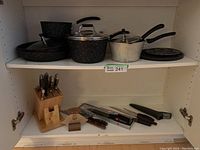 Wide view of upper and lower kitchen cabinet shelf with pots, pans, knife block, loose knives, and pot stands.