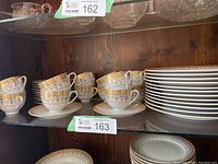 Photo showing 12 Royal Vienna China cups stacked on matching saucers next to a stack of 12 dinner plates, all on glass shelving.