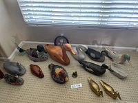 Overview of 12 duck figurines arranged on carpeted floor with clock behind them.