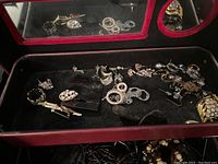 Open jewelry box tray with a variety of earrings including hoop, stud, and decorative rhinestone styles arranged on black fabric.