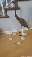 Overall view showing the large wicker blue heron statue and three smaller white wooden shorebird figures on stands arranged on a wood floor near a staircase.