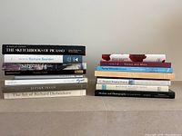 Two stacks of art books on a flat surface, titles visible including Picasso, Romare Bearden, Sargent, Klimt, Lucian Freud, Richard Diebenkorn among others.