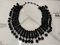 Full view of the black faceted glass bead collar necklace sculpted with multiple strands and dangling beads.