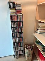 Photo of tall black metal CD stand filled with multiple CDs with a paper bag holding more CDs beside it.