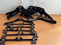 Overview of the 15 Chanel velvet hangers arranged on a wooden surface including 10 dress hangers and 5 pant clip hangers, showing gold Chanel logos and gold hooks.
