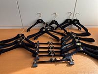 Full view of 19 black velvet hangers, 14 are dress hangers and 5 pant clip hangers, all have gold hooks and gold double C logo