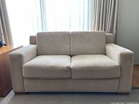 Front view of beige chenille loveseat centered against a window