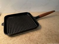 Full view of Copco cast iron grill pan showing square shape, ribbed cooking surface and wooden handle.