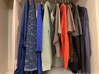 Front view of nine ladies sweaters hanging on a rack showing various colors and textures.