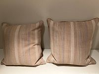 Two striped decorative throw pillows side by side on white surface against neutral wall