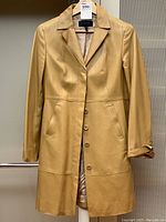Front full view of camel leather coat on hanger showing notch lapel, button closure, and overall condition.