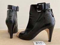 Side-by-side view of both boots showing black leather upper, cream toe cap, quilted heel, strap and buckle