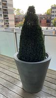 Artificial pyramidal boxwood in large gray resin planter positioned on balcony.