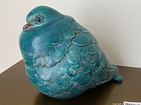 Front angled view of the blue ceramic bird sculpture showing rounded form, textured and scalloped feathers, and facial details.