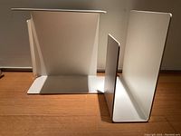 Two white lacquered steel pieces (table and magazine rack) on wooden floor against a wall