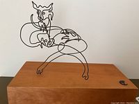 Front view of wire devil sculpture on wood base.