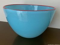 Blue art glass bowl with a glossy finish and a red rim. Photograph from an angled side view showing the shape and colors.