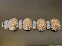 Top-down view of the bracelet showing the textured gold tone large sections and rhinestone encrusted smaller segments.