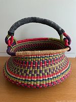 Front view of colourful woven basket showing round shape and leather handle