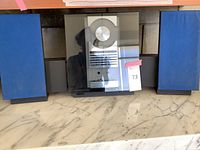 Central stereo unit with tinted glass front, aluminum knob and button array visible, flanked by blue grille speakers