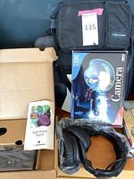 Image shows IBM PC camera in original box, Apple Product Support manual, black computer cases, and headphones.