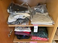 Collection of folded men’s sweaters and sweatshirts on wooden shelves, some wrapped in plastic.