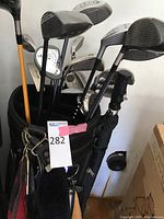 Golf clubs in black golf bag showing various clubs by Callaway, Adams, Spalding, and others with club covers and some grips visible.