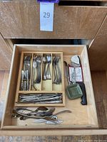 Top view of a drawer showing organized flatware with forks, spoons, assorted utensils, and pewter spreaders including one with a black handle.