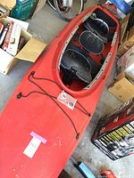 Full-length top view of red kayak showing two cockpit openings, deck bungee cords and overall condition