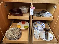 Wide view of kitchen cabinet shelving with bowls, plates, utensils, salad spinner, and chip dip bowl