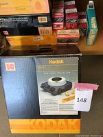 Photo of Kodak Carousel Model EKTAMATIC III projector box showing image of projector and carousel tray, along with various slide trays and Kodak slide boxes in the background.