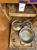 Photo of stainless steel pot with strainer and two glass lids in wooden drawer