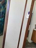 Full view of one speaker panel showing beige fabric grille, wood side rails, approximate height and width.