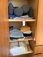 Neck cushions stacked horizontally above folded men's clothing including shirts and pants in blue, mustard, and patterned styles on middle wooden shelf.