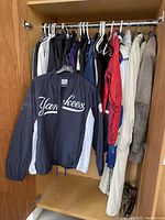Multiple men's jackets on hangers showing navy Yankees windbreaker at front and assorted athletic jackets behind