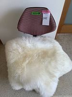 Top view of rose colored office chair backrest with size label and sheepskin rug draped over it.
