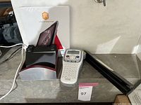 Photo showing a Brother P touch label maker, a photo frame stand with display box, and a long black item (possibily frame stand or case)