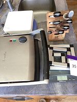 Breville panini press closed with handle, knife block with cutting knives and knives sharpening steel, Salter digital kitchen scale, and white plastic plates are seen on counter