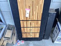 Top-down view of disassembled shuffleboard table board on black base with scoring zones and shuffleboard pucks