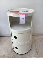 Full view of white round storage end table showing two sliding compartments, open middle shelf, and smooth round top.