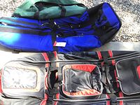 Three travel bags including two golf club travel bags and one large green duffel bag placed outdoors on concrete and gravel.